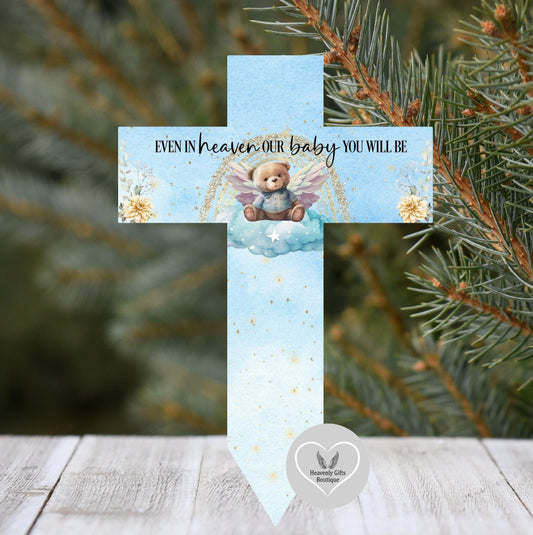 Memorial cross with teddy bear design and text 'EVEN IN HEAVEN OUR BABY YOU WILL BE' against a Christmas tree background.