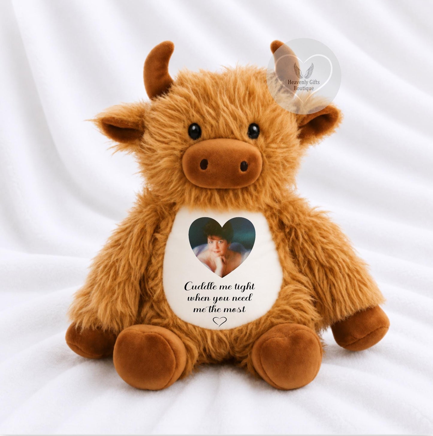 A fluffy brown plush cow bear. The cow has a white belly patch with a heart-shaped photo with printed message 'Cuddle me tight when you need me the most'.