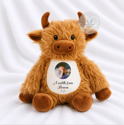 A fluffy brown plush cow toy, with a custom photo printed on its belly that reads 'A cuddle from Heaven'.