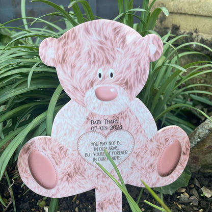 Pink teddy bear grave marker shown beside flowers for scale