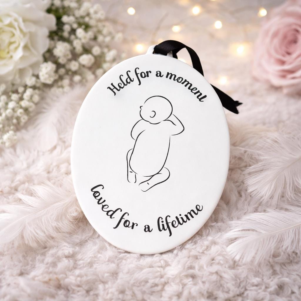 Baby loss hanging decoration with black ribbon displayed beside pink and white flowers