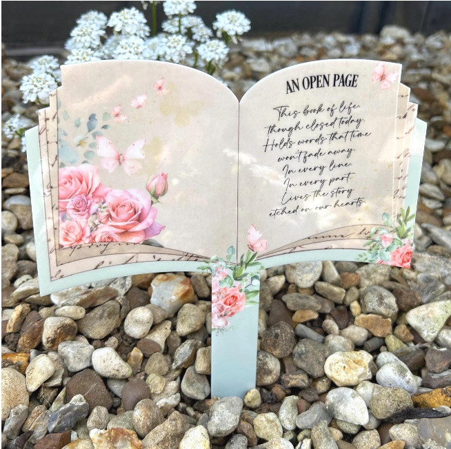 Pink rose and butterfly open book grave marker featuring the An Open Page memorial poem in an outdoor graveside setting