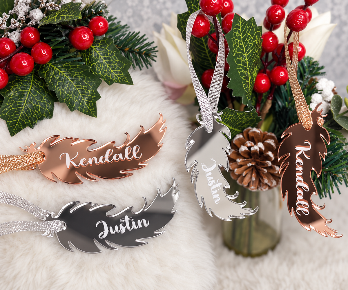 Personalised silver and rose gold mirror feather memorial Christmas decorations with names, displayed with festive foliage