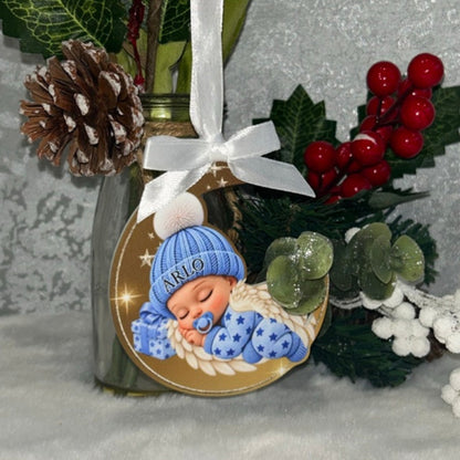 Real photograph of blue Sleeping Angel Baby memorial bauble with optional name Arlo, white ribbon and bow, displayed beside festive berries and white flowers.